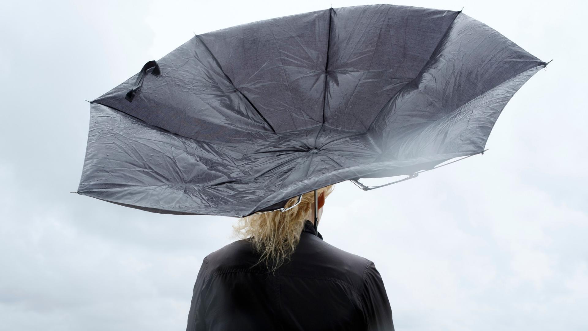 Frau mit Regenschirm, der vom Wind erfasst wird