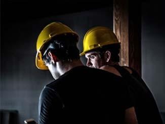 Zwei Bauarbeiter sind auf einer Baustelle, die schlecht beleuchtet ist.