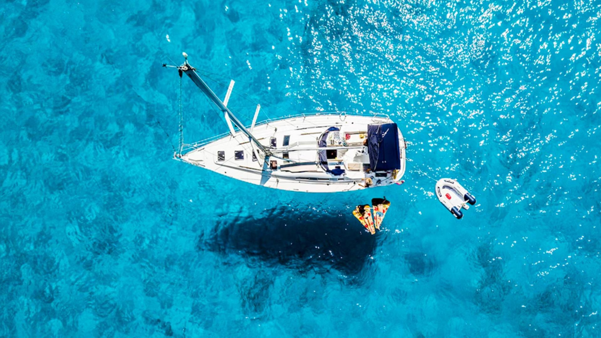 Zwei Personen auf Luftmatratzen schwimmen neben einem Segelboot