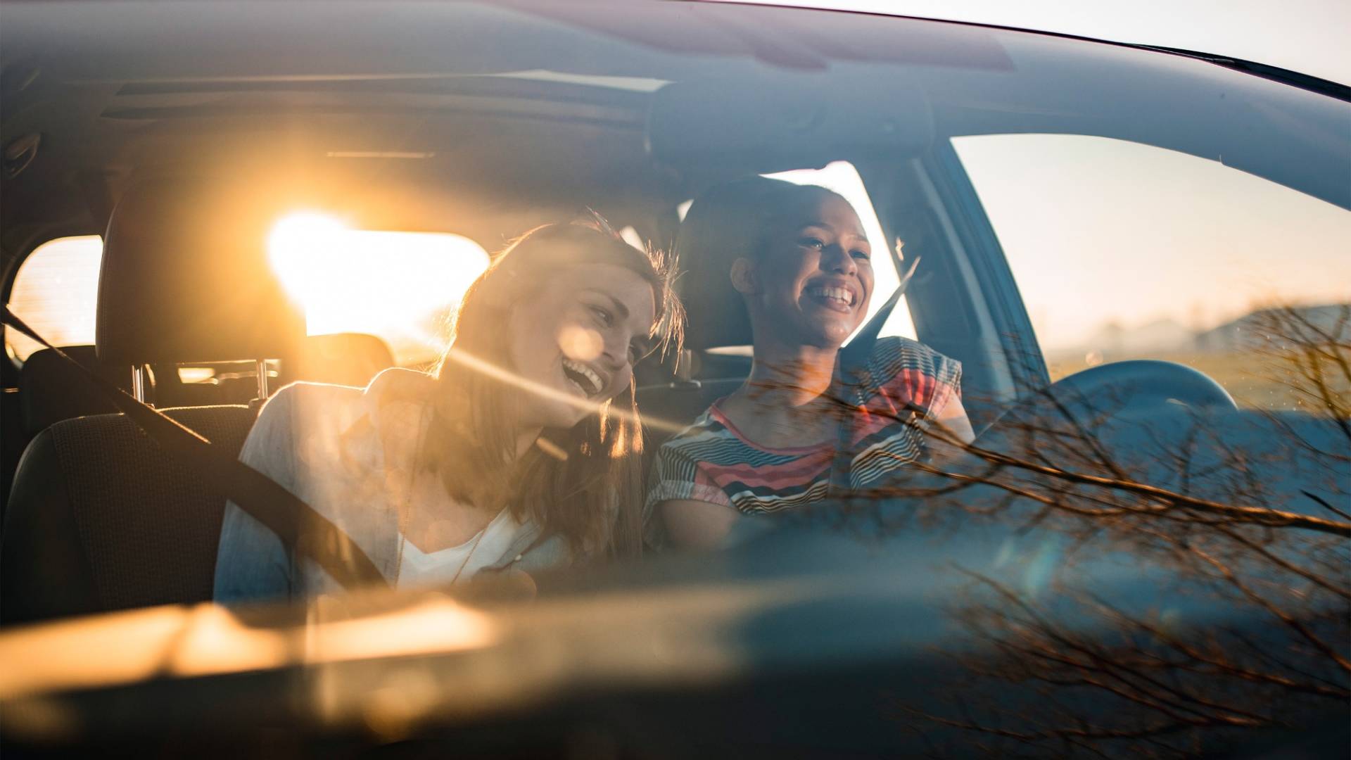 Auto mit einer defekten Frontscheibe. Im Hintergrund befindet sich eine ratlose Frau am Telefon.