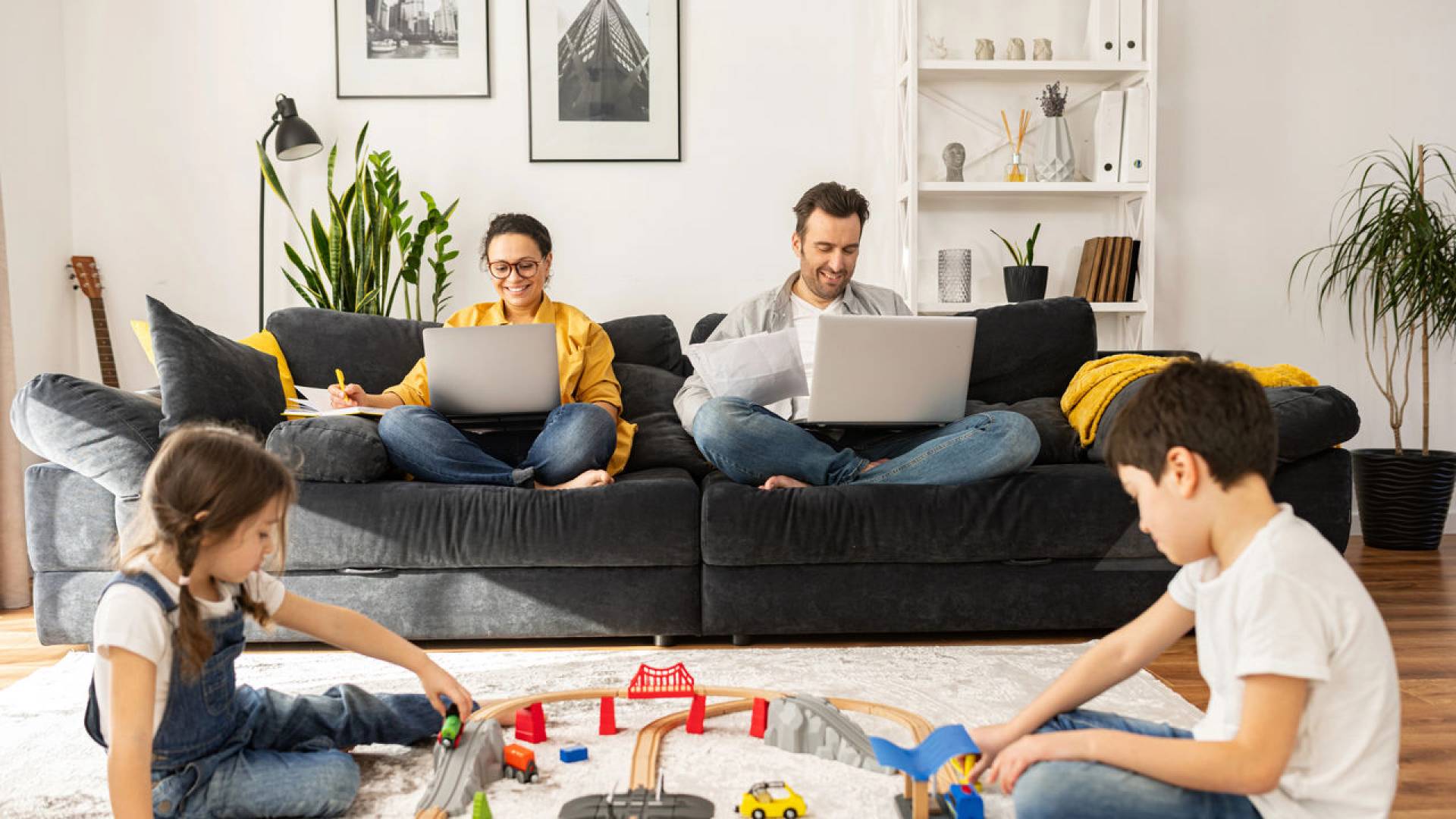 Busy parents work remotely with laptops sitting on the couch in living room