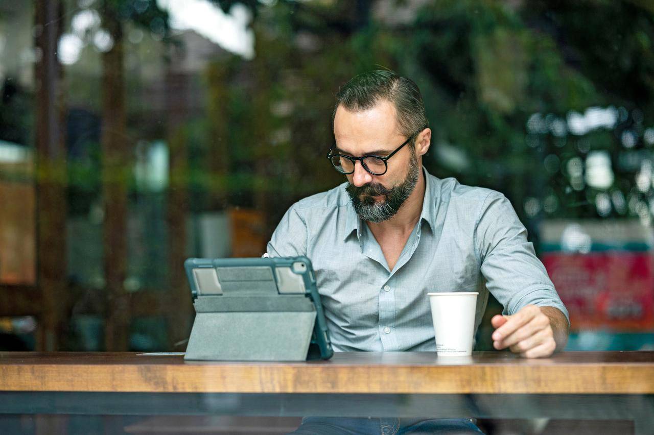 Front View of a Confidence man working online at a cafe using a digital tablet. Portability, Flexibility, City life.