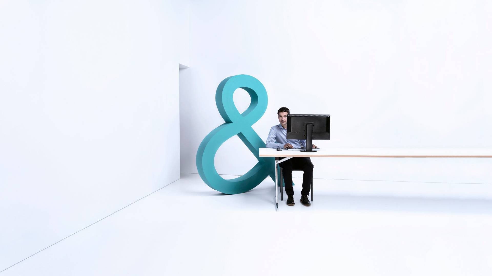 A man sitting in a white room at a computer. 