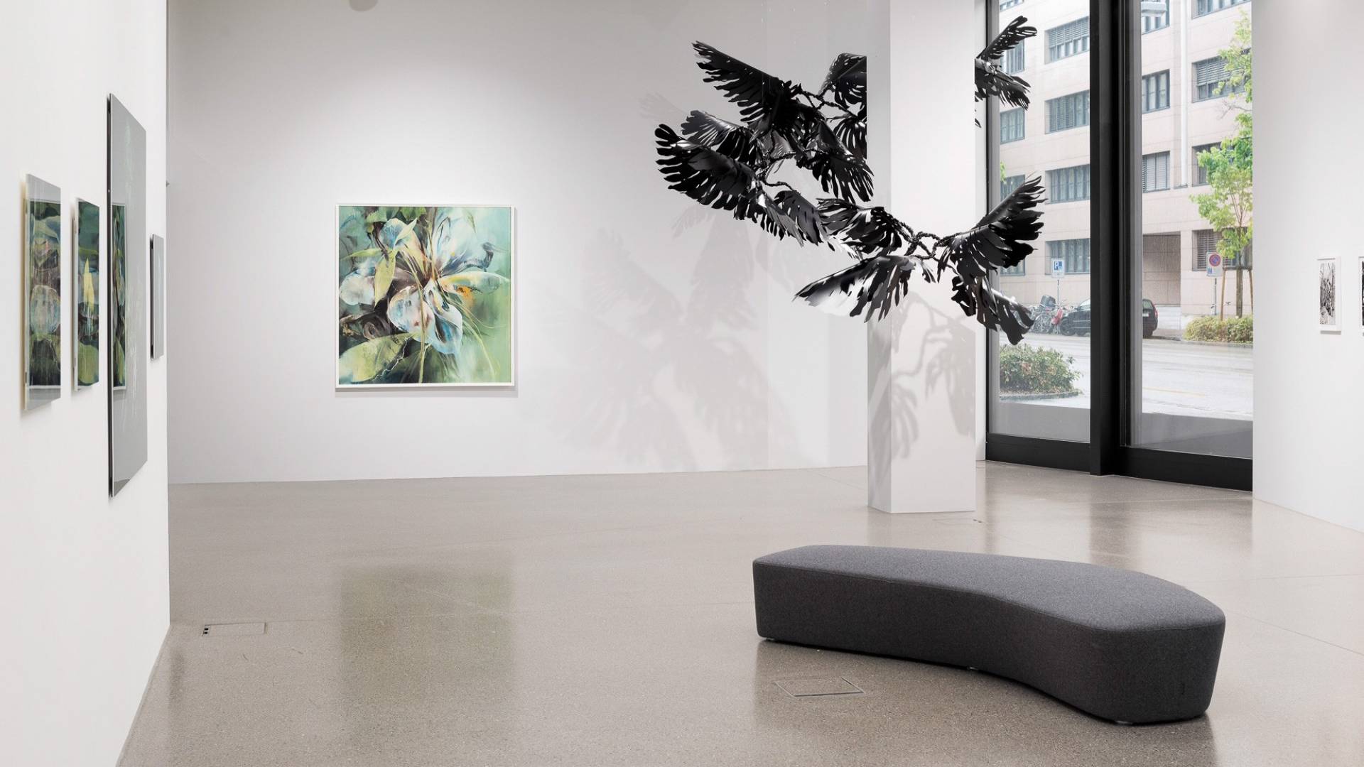 “Monstera” – the decorative indoor plant created by Franziska Furter in black PVC floats in the room, suspended on nylon threads. A painting by Basel artist Helmuth Mahrer hangs on the back wall.