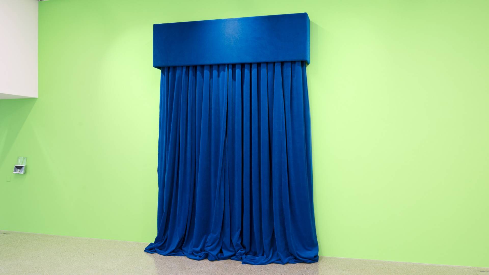 Blue, heavy looking velvet curtain in front of a green painted wall.