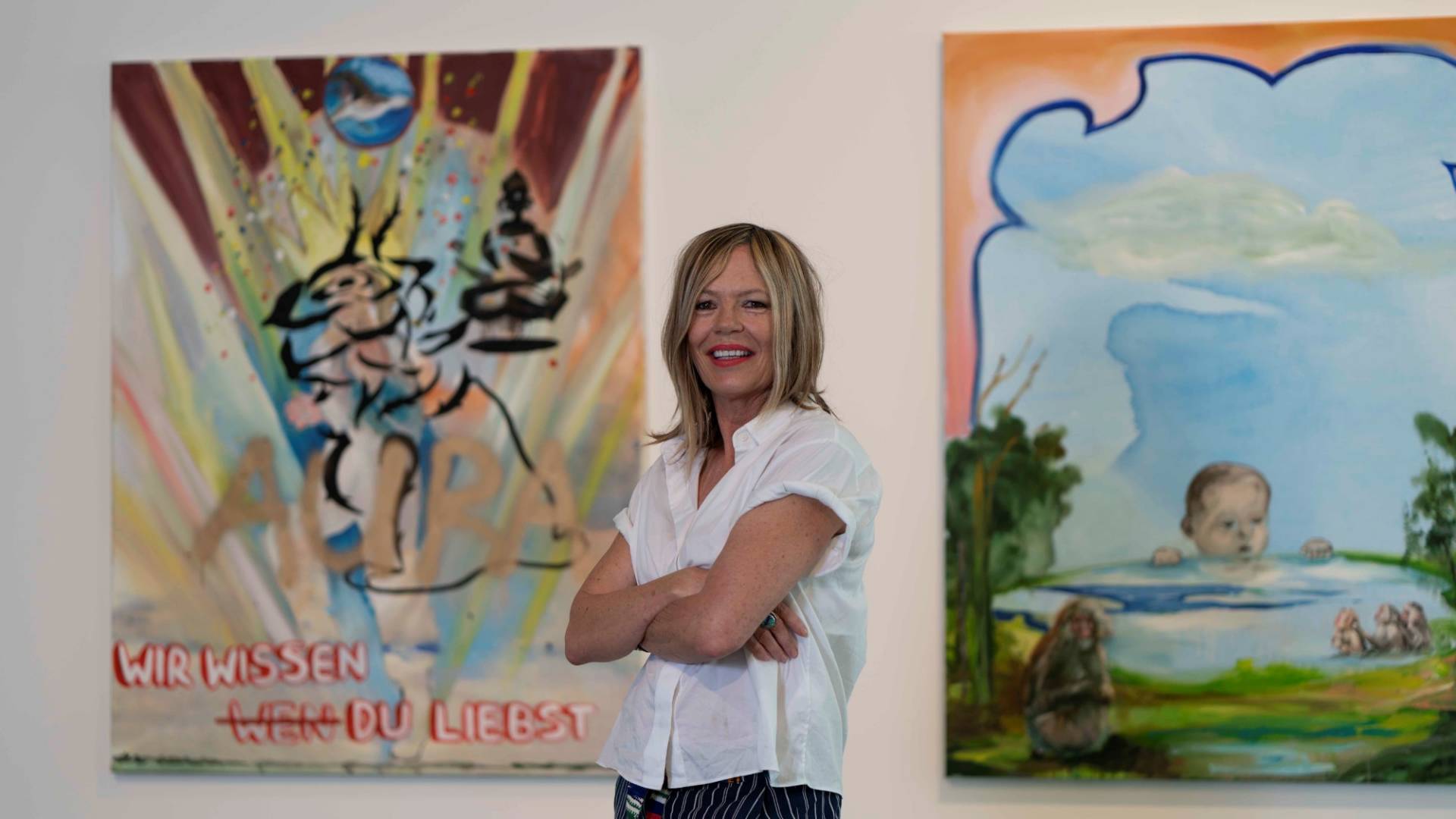The artist flanked by two of her paintings. They are brightly painted canvases.