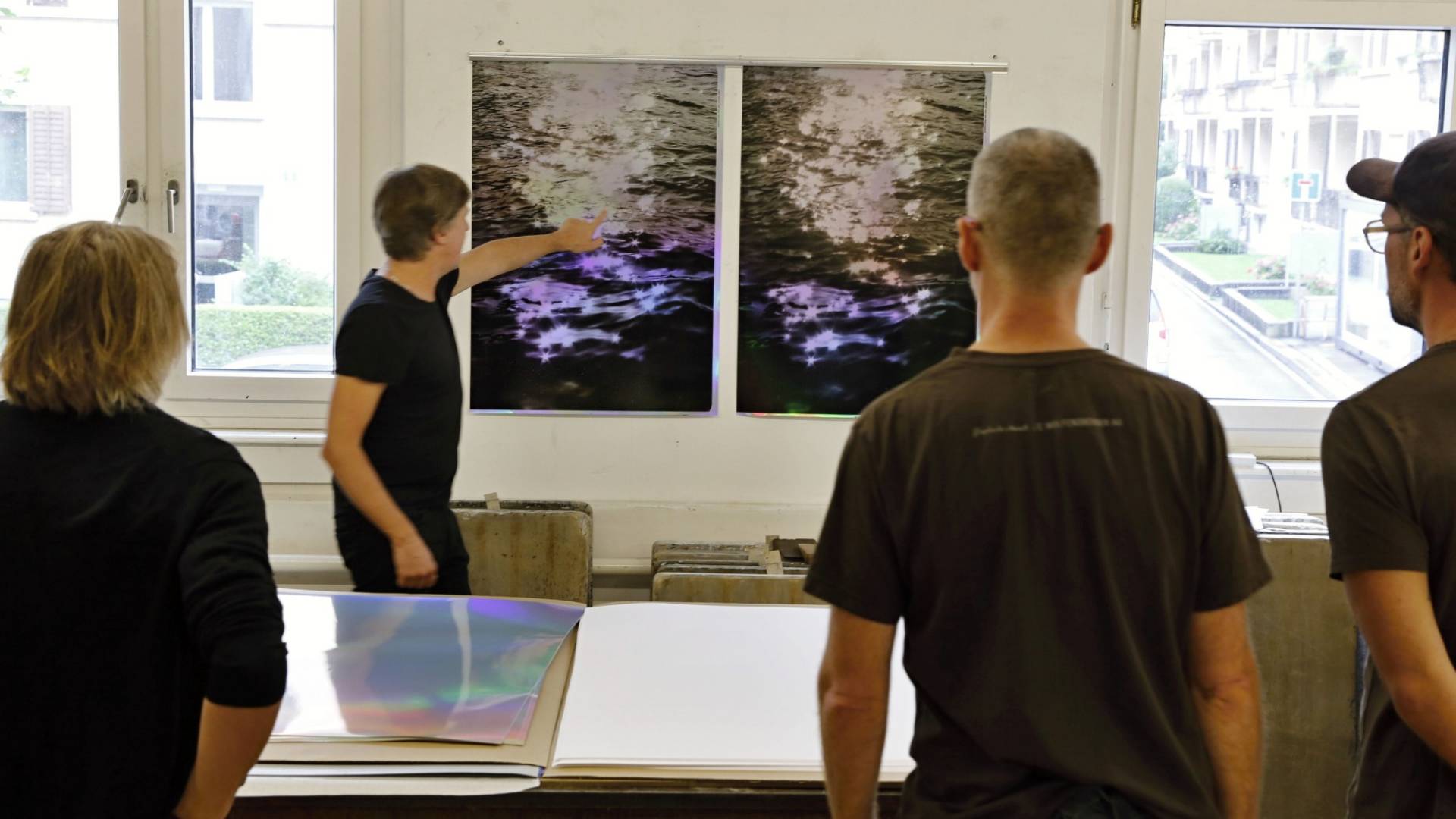 Two printouts of the "stella maris" graphic artwork on the wall. Four people are standing in front of it and examining the art print.
