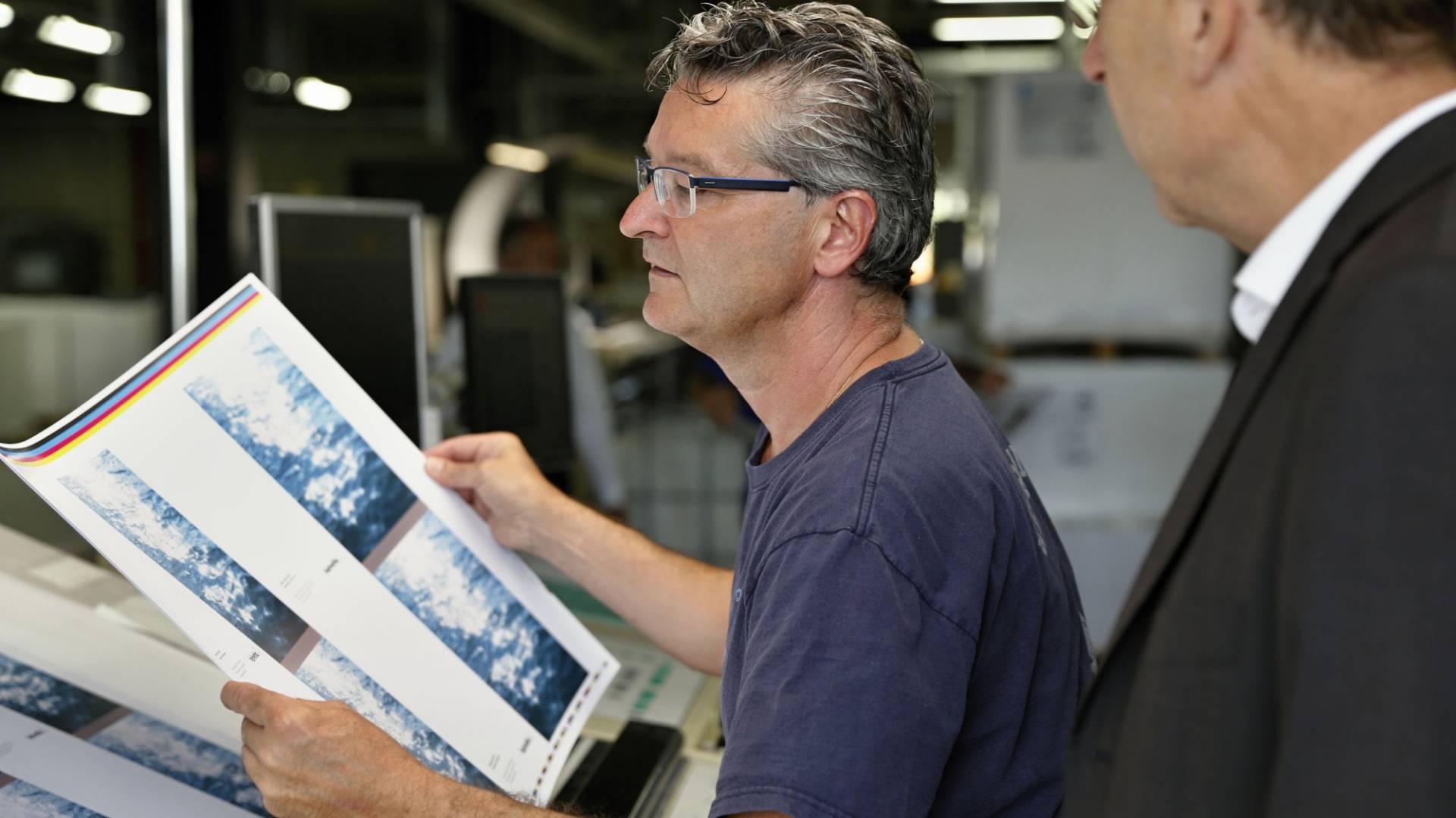 A man holds a printout of the artwork while another man looks over his shoulder.