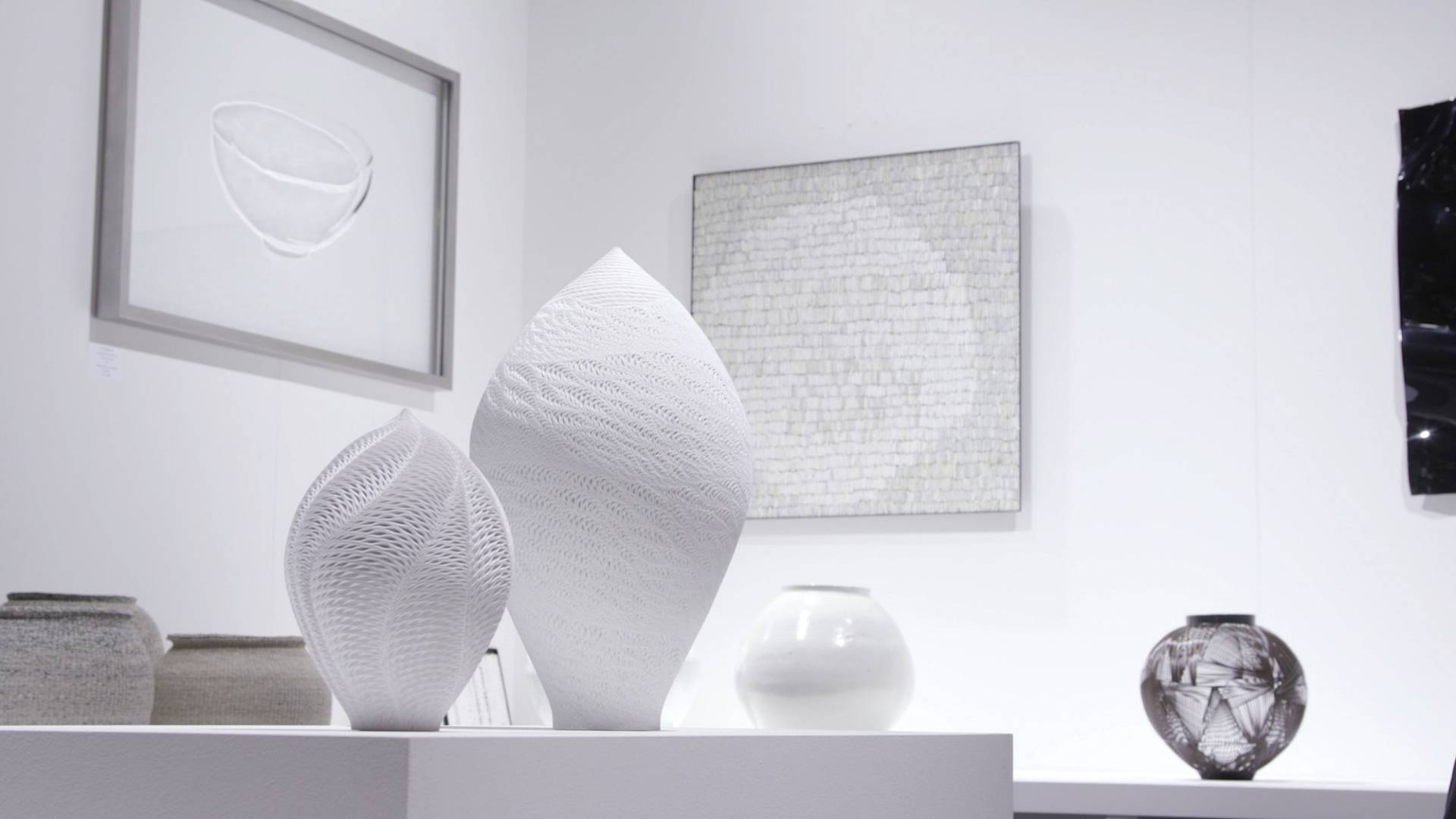 Exhibition stand with ceramic sculptures in white-and-grey tones, vases and wall art.