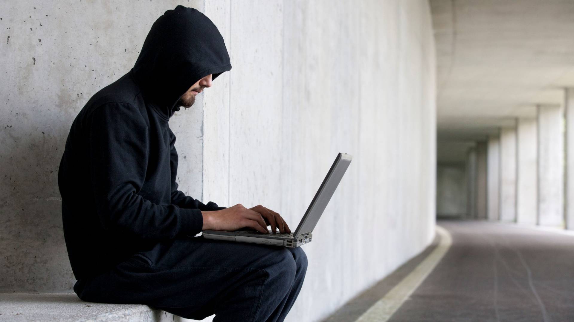 Man with black hood sits at his laptop 