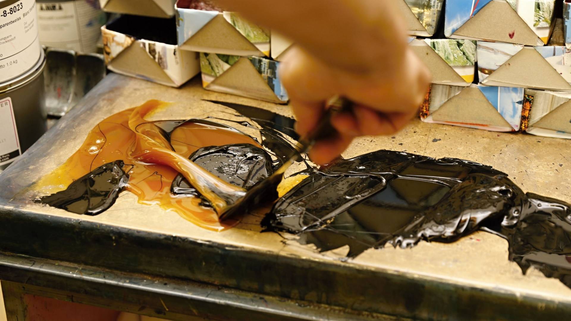 De la peinture noire et de la peinture dorée sont mélangées à l’aide d’une spatule.