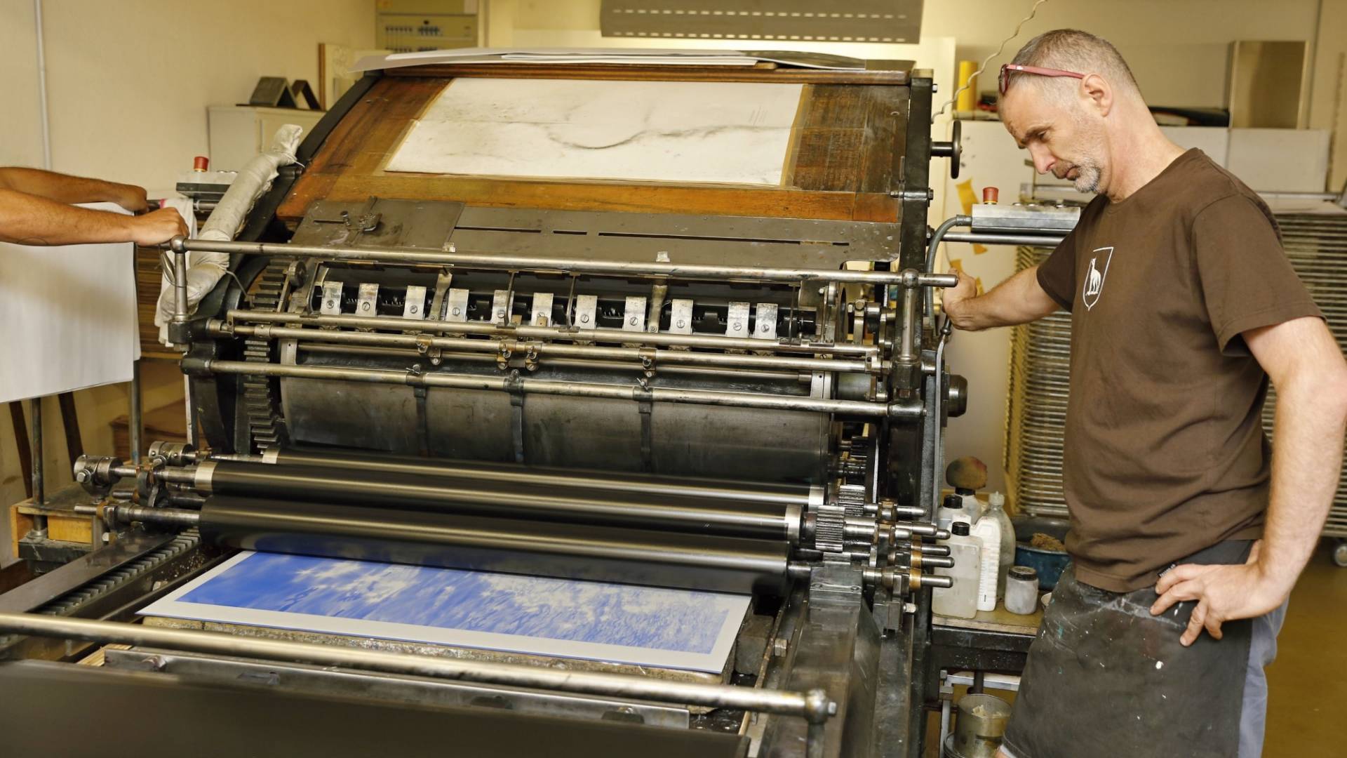 Un homme debout à côté d’une presse lithographique .