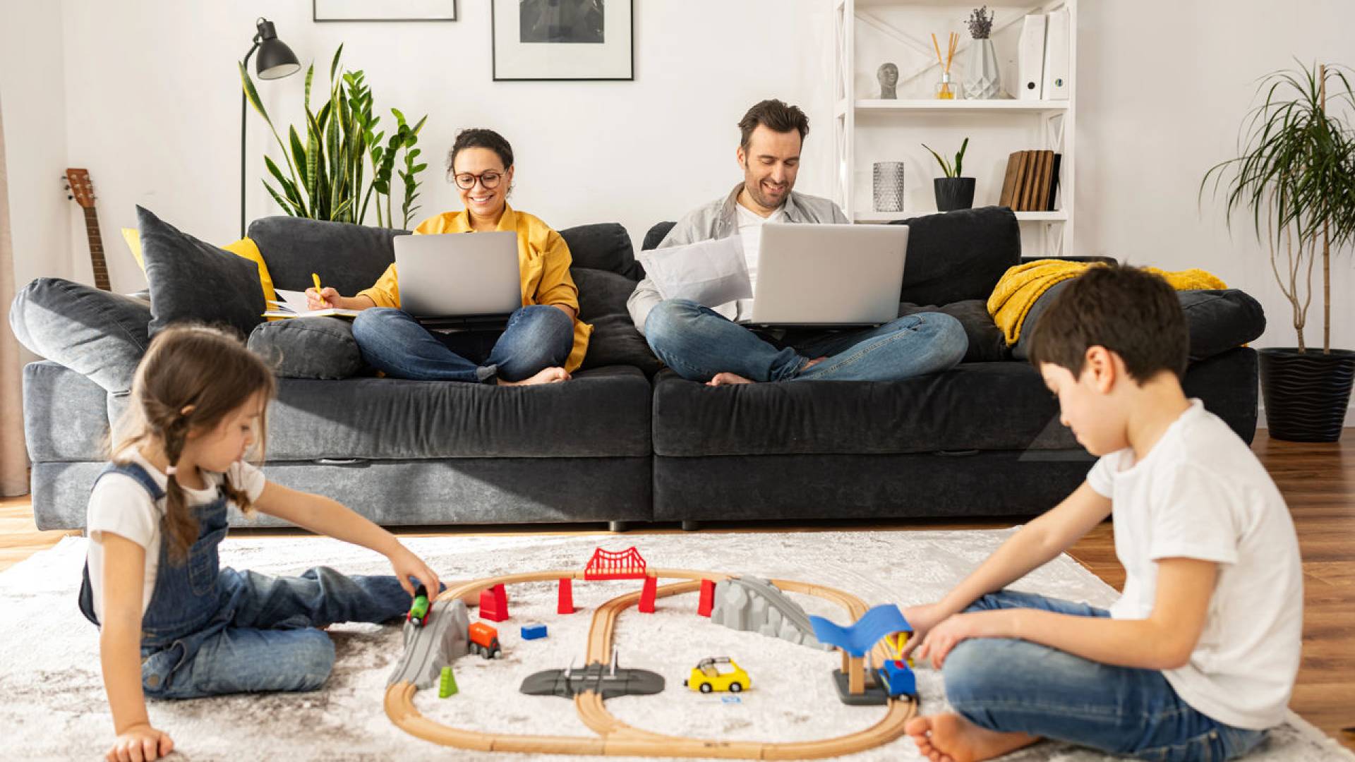 Busy parents work remotely with laptops sitting on the couch in living room