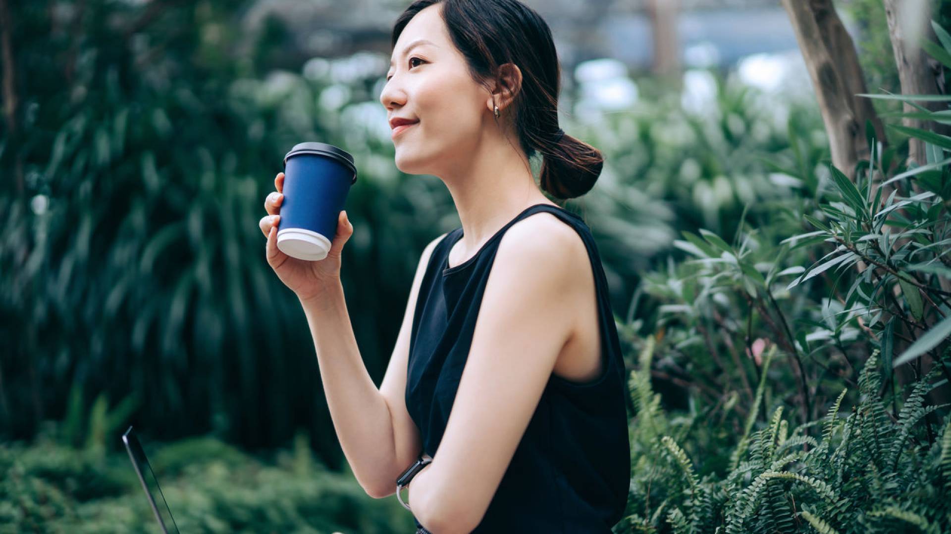 Una donna con una tazza di caffè in mano è in piedi nella serra.