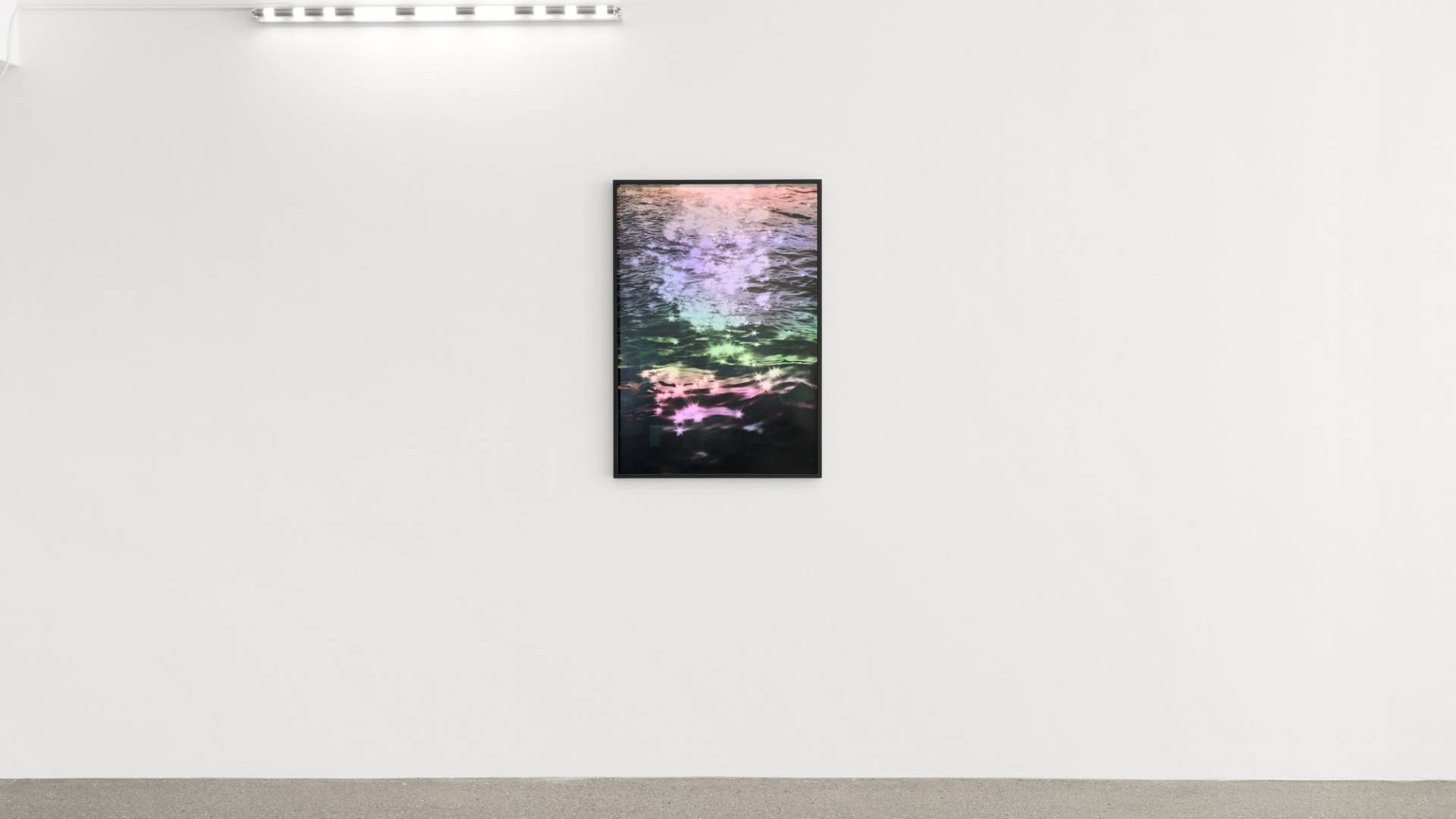 Al centro è appesa un’immagine che riproduce le increspature variegate e brillanti della superficie del mare. Sopra di essa, sulla sinistra, un tubo fluorescente che proietta il segnale internazionale di soccorso in alfabeto Morse SOS.