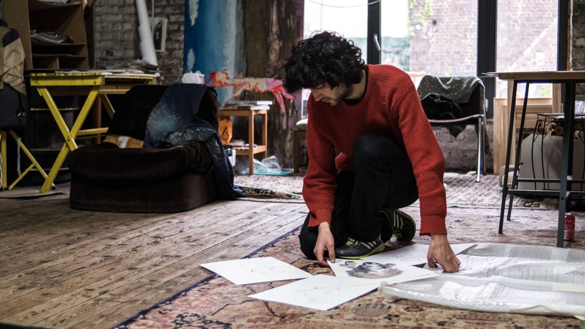 Andriu Deplazes, in ginocchio sul pavimento del suo atelier, classifica e osserva gli schizzi che ha disegnato a china su fogli bianchi.