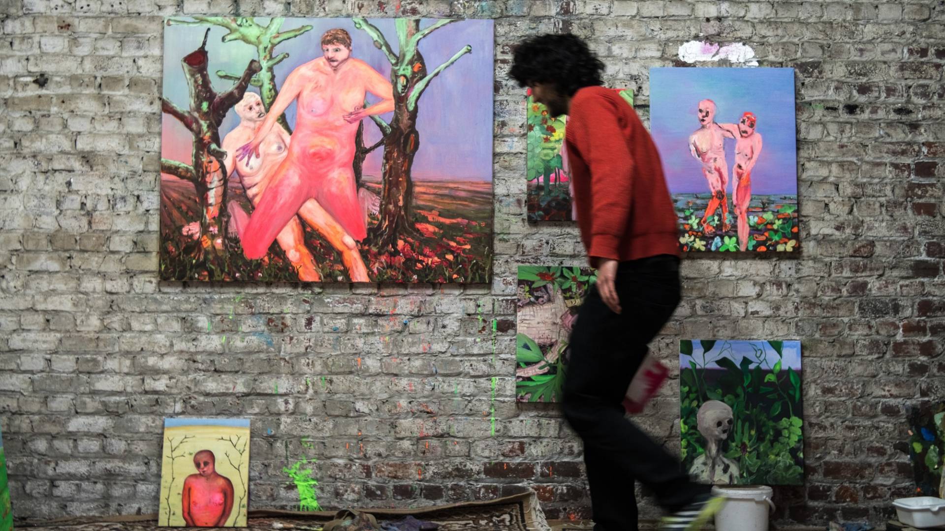 Andriu Deplazes carries a picture to a brick wall in his studio, where several pictures have already been hung. He has painted the pictures using oils in brilliant colours.