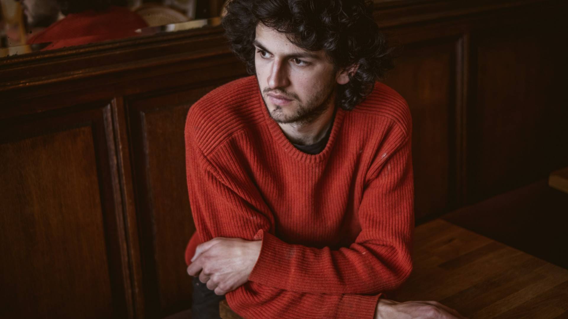 Il giovane artista Andriu Deplazes seduto in un caffè a Bruxelles mentre guarda pensoso fuori dalla finestra.