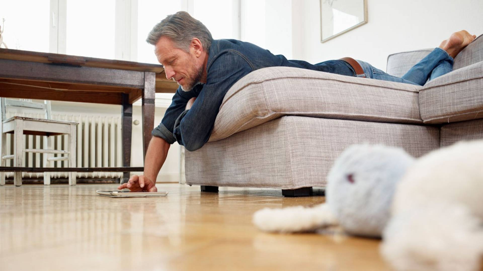 Un pensionato è disteso su un divano e legge in uno smartphone. 