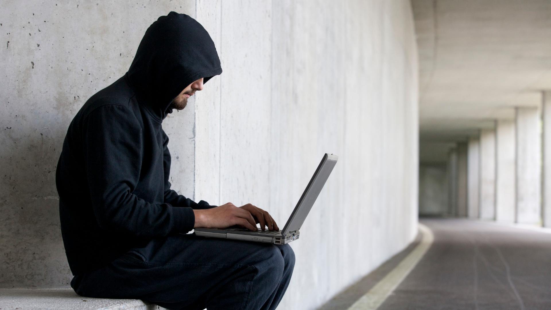 Hacker with laptop sitting in an underground car park