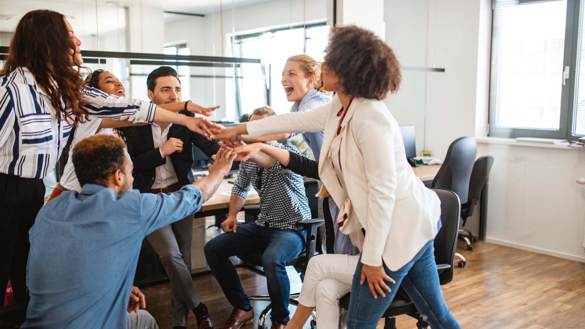Mehrere Personen stehen in einem Büro im Kreis und legen die Hände übereinander.