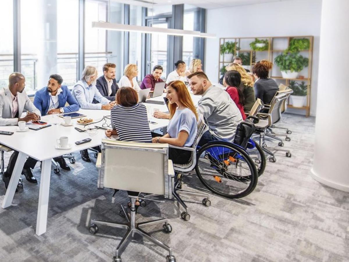 Um einen Konferenztisch sitzen mehre Personen, unter ihnen befindet sich auch ein Mann im Rollstuhl.