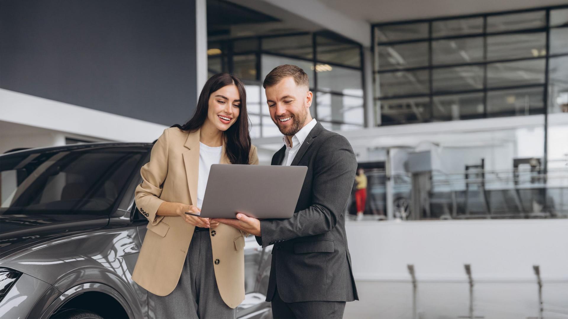 Mann und Frau stehen vor einem Auto  und blicken auf einen Lapotop.