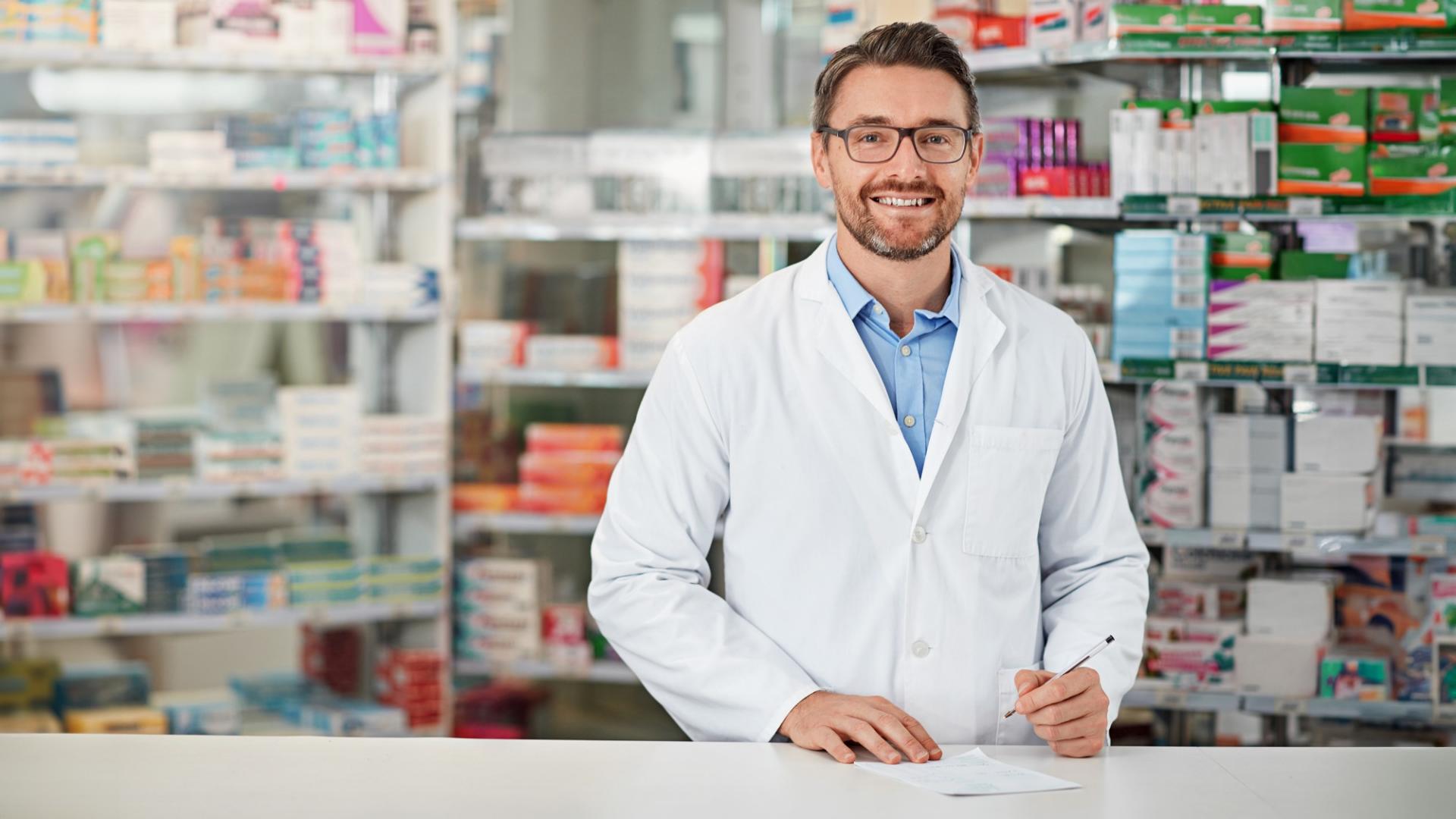 Ein Mann mit weißem Kittel steht vor einem Regal mit Medikamenten