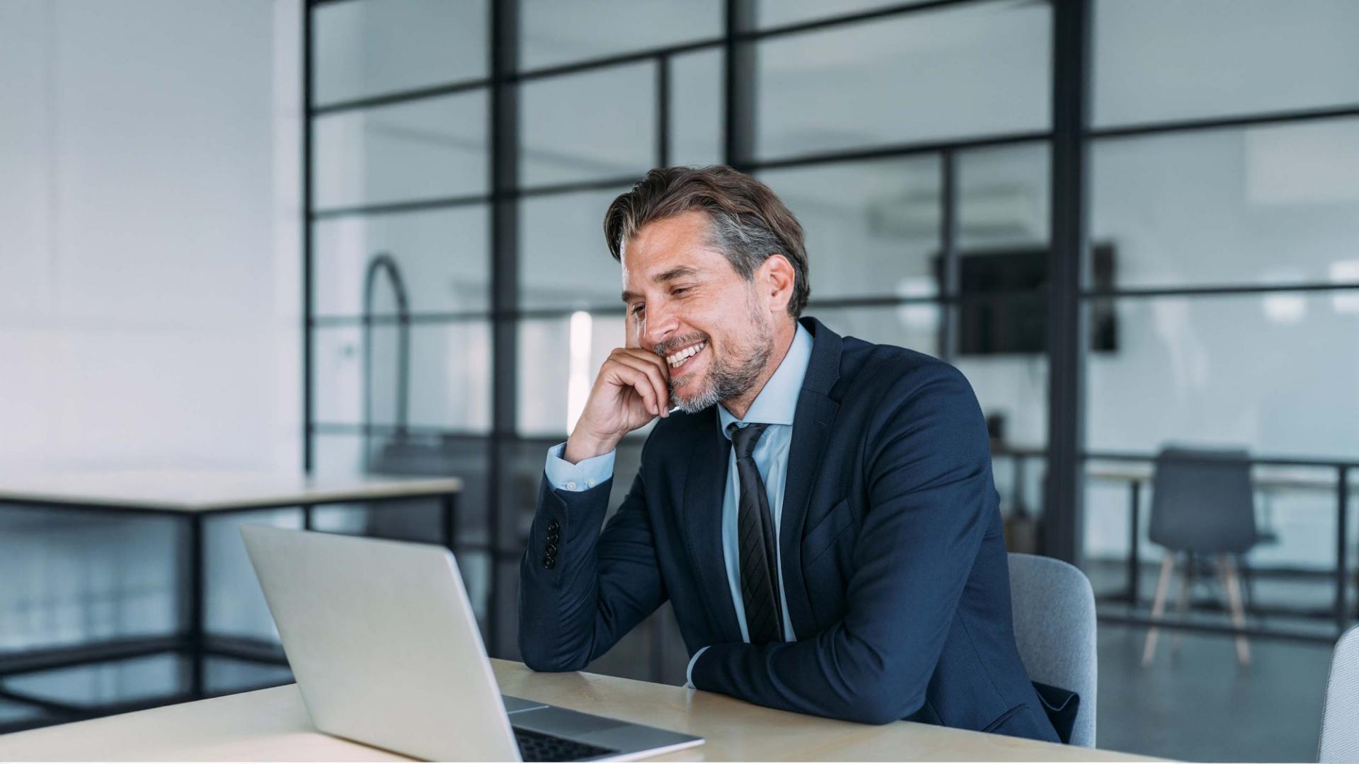 Mann mit Dreitagebart in Geschäftskleidung sitzt vor einem Laptop.