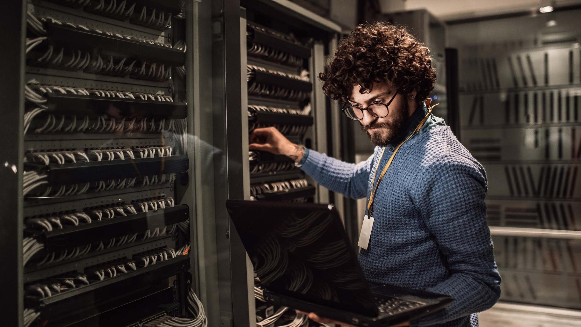 Ein Mann mit Laptop steht im Serverraum.