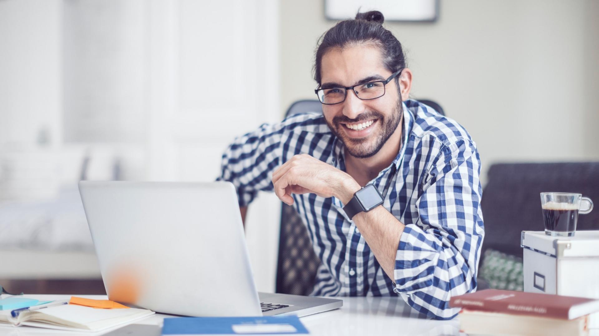 Mann mit kariertem Hemd und Brille vor einem Laptop