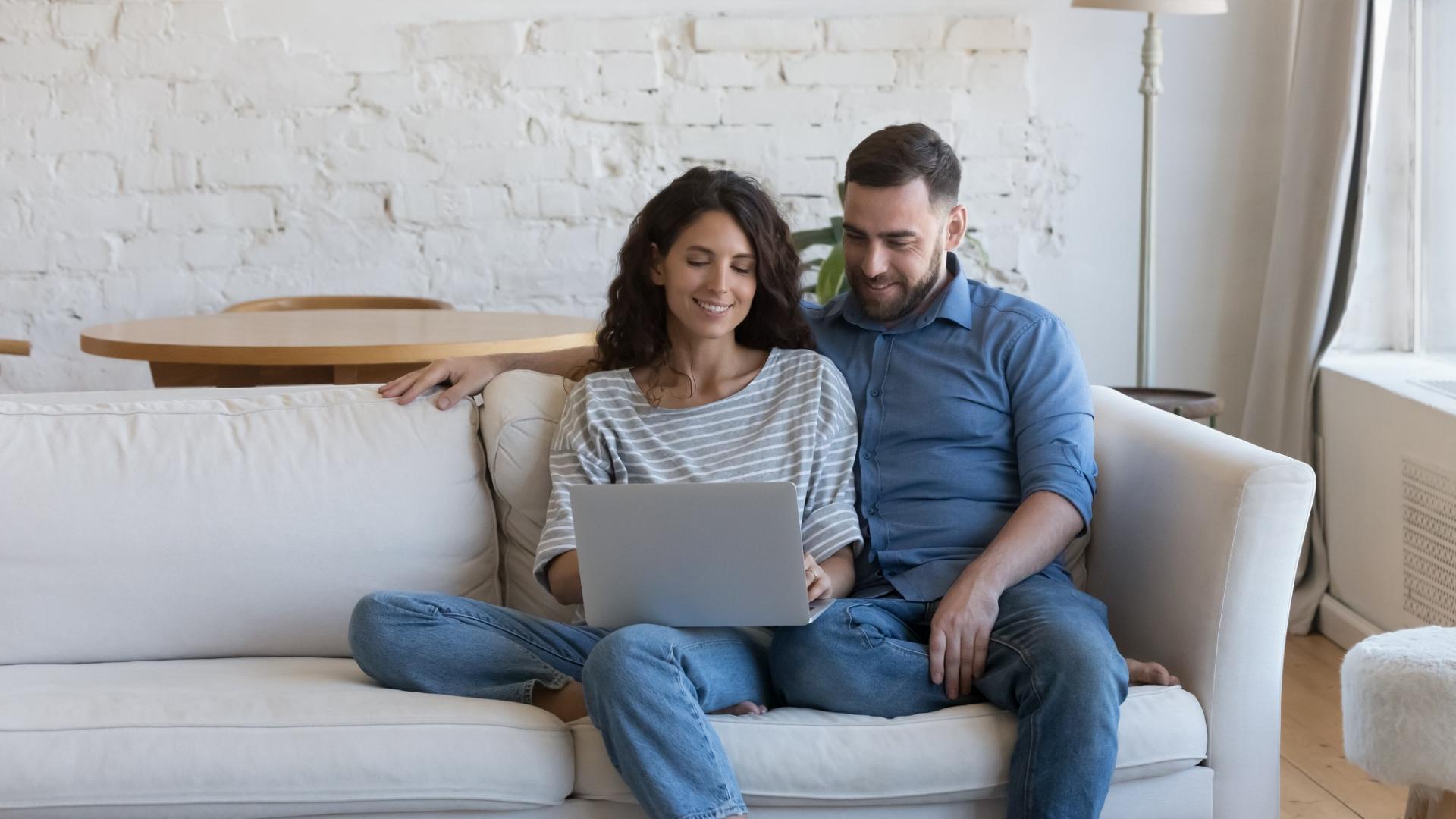 Eine Frau und ein Mann sitzen zusammen auf einer Couch und schauen in einen Laptop.