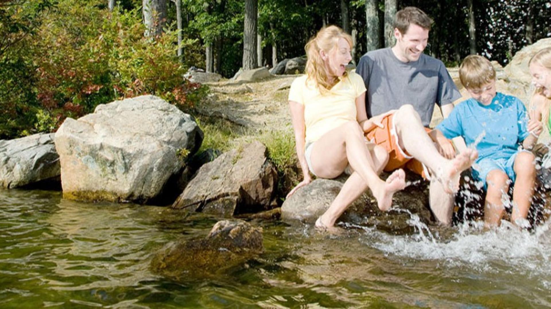 Eine Familie sitzt auf Steinen am einem Fluss und hat die Füße im Wasser