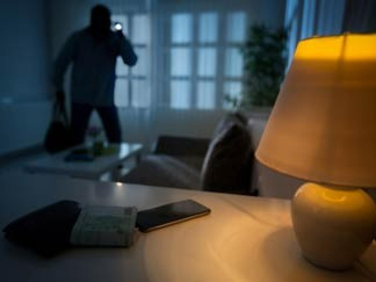 Ein Einbrecher läuft im Dunkeln mit einer Taschenlampe in der Hand durch eine Wohnung.