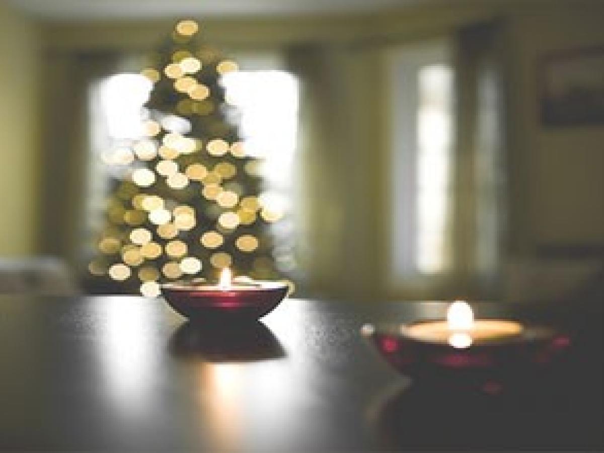 Brennende Teelichte stehen vor einem Weihnachtsbaum auf dem Tisch.