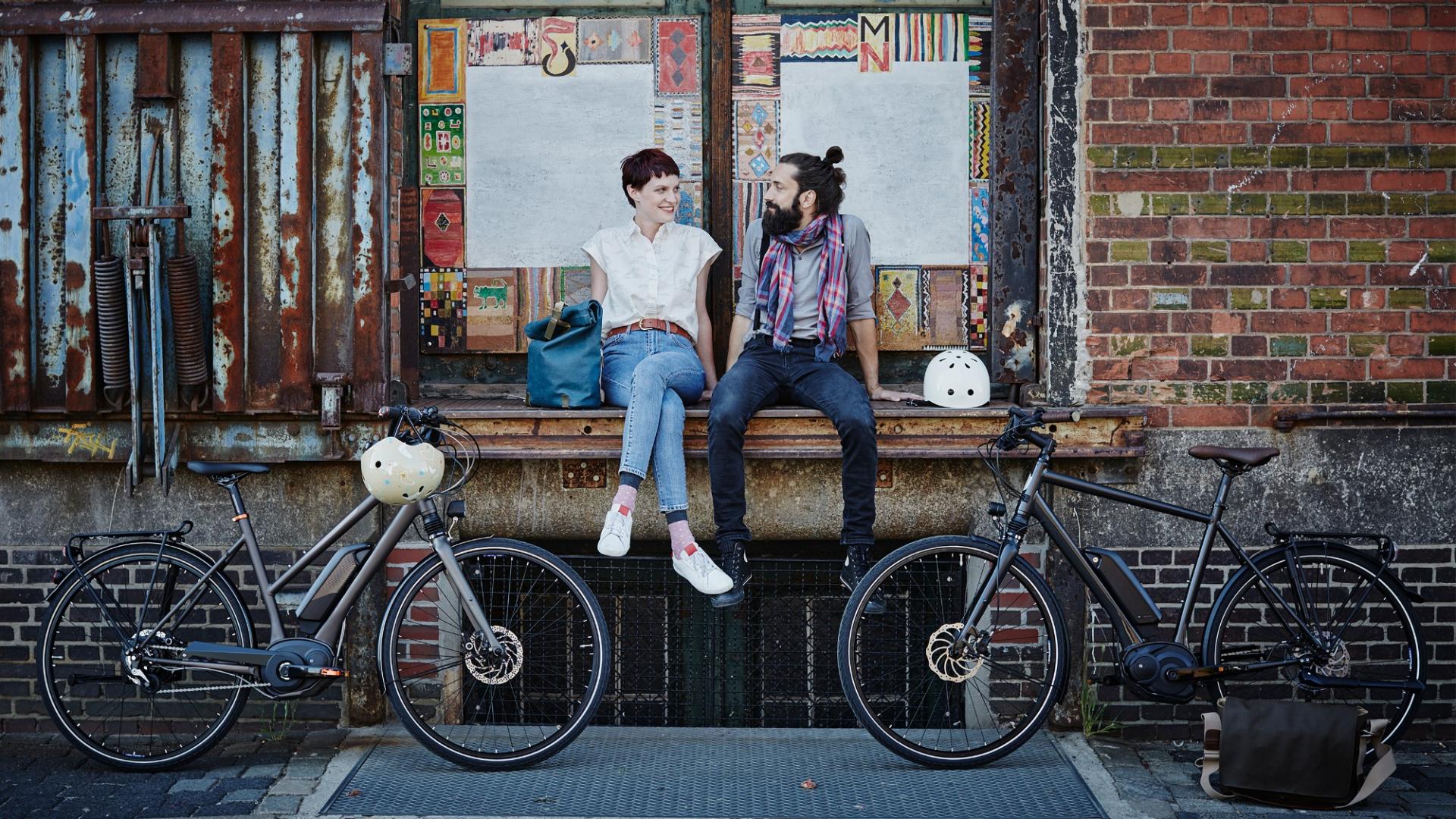 Ein Mann und eine Frau sitzen auf einem Fensterbrett und davor stehen zwei e-Bikes