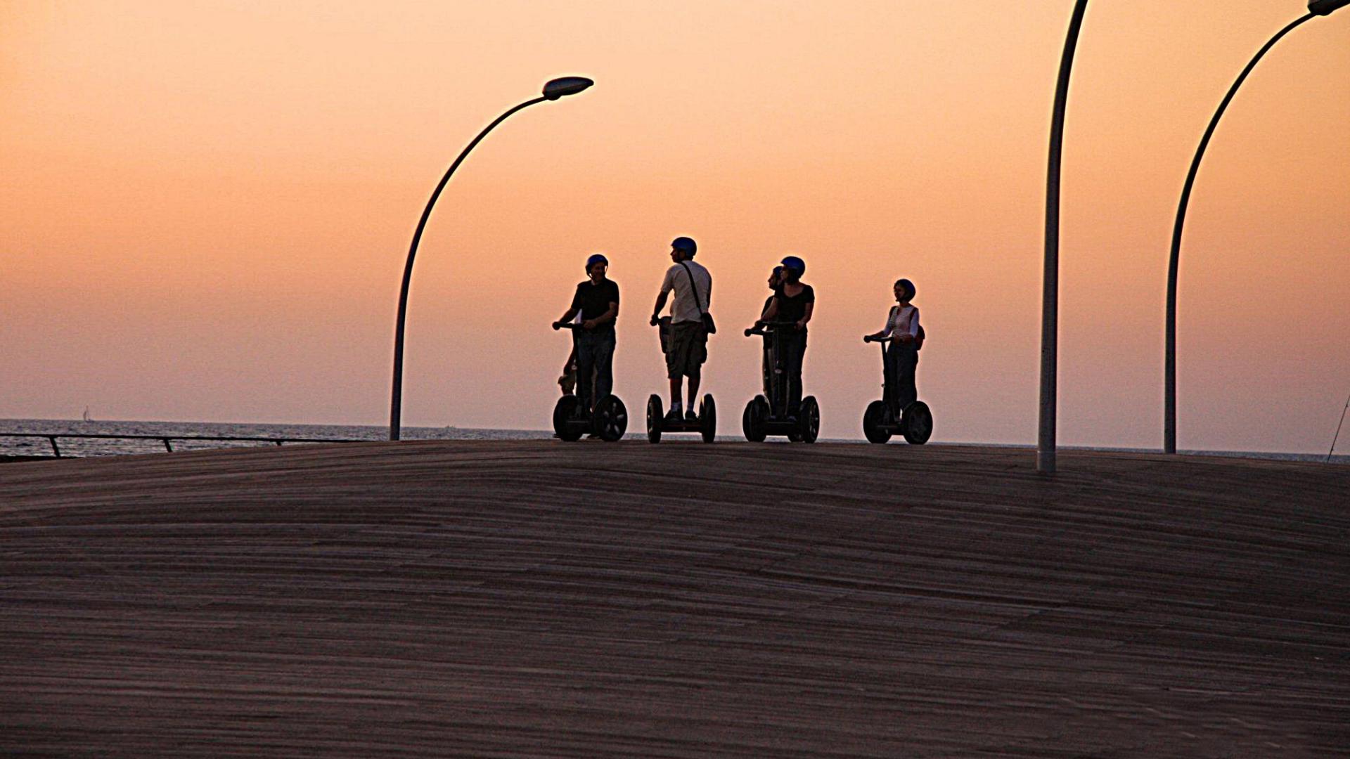 Vier Personen fahren mit Segways Richtung Sonnenuntergang.