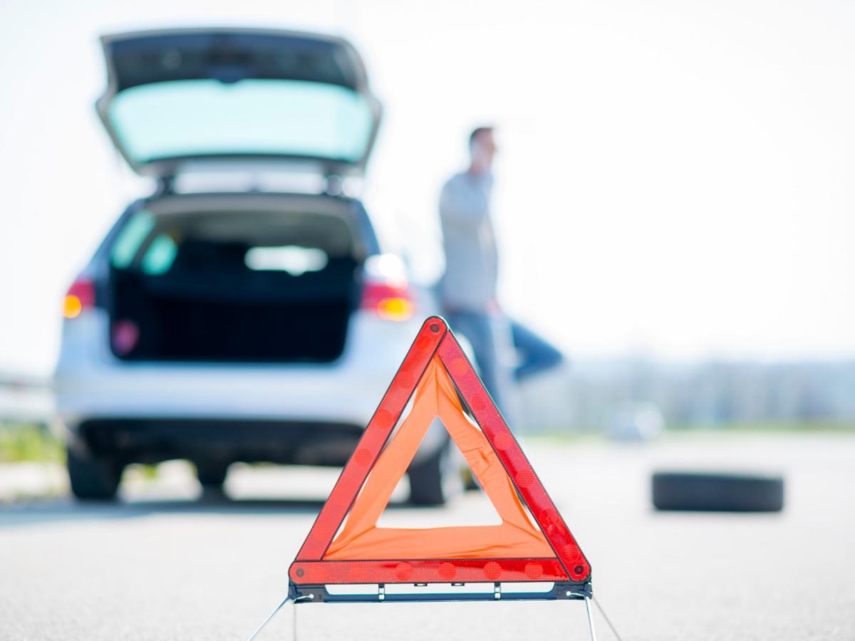Ein Auto hat eine Panne und hat den Kofferraum offen und ein Warndreieck aufgestellt.
