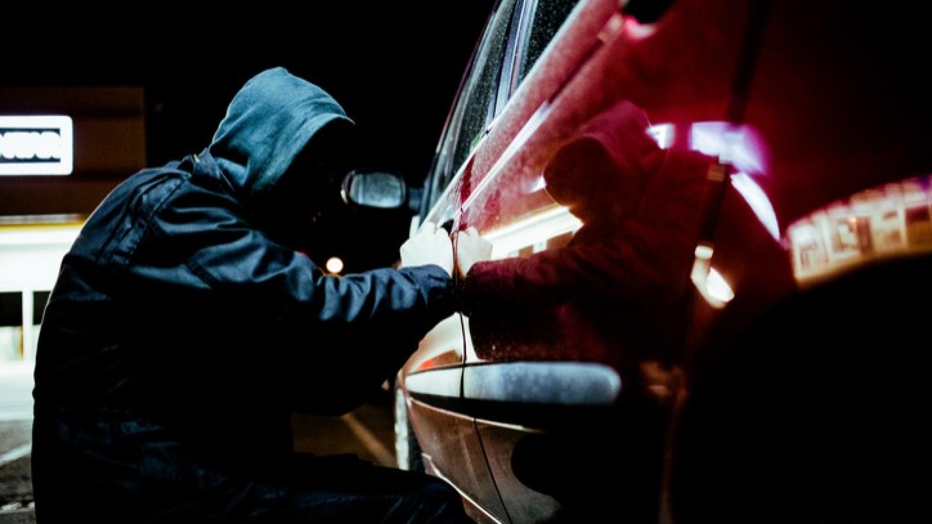 Ein Mann mit Hoodie probiert in der Nacht in ein rotes Auto einzubrechen