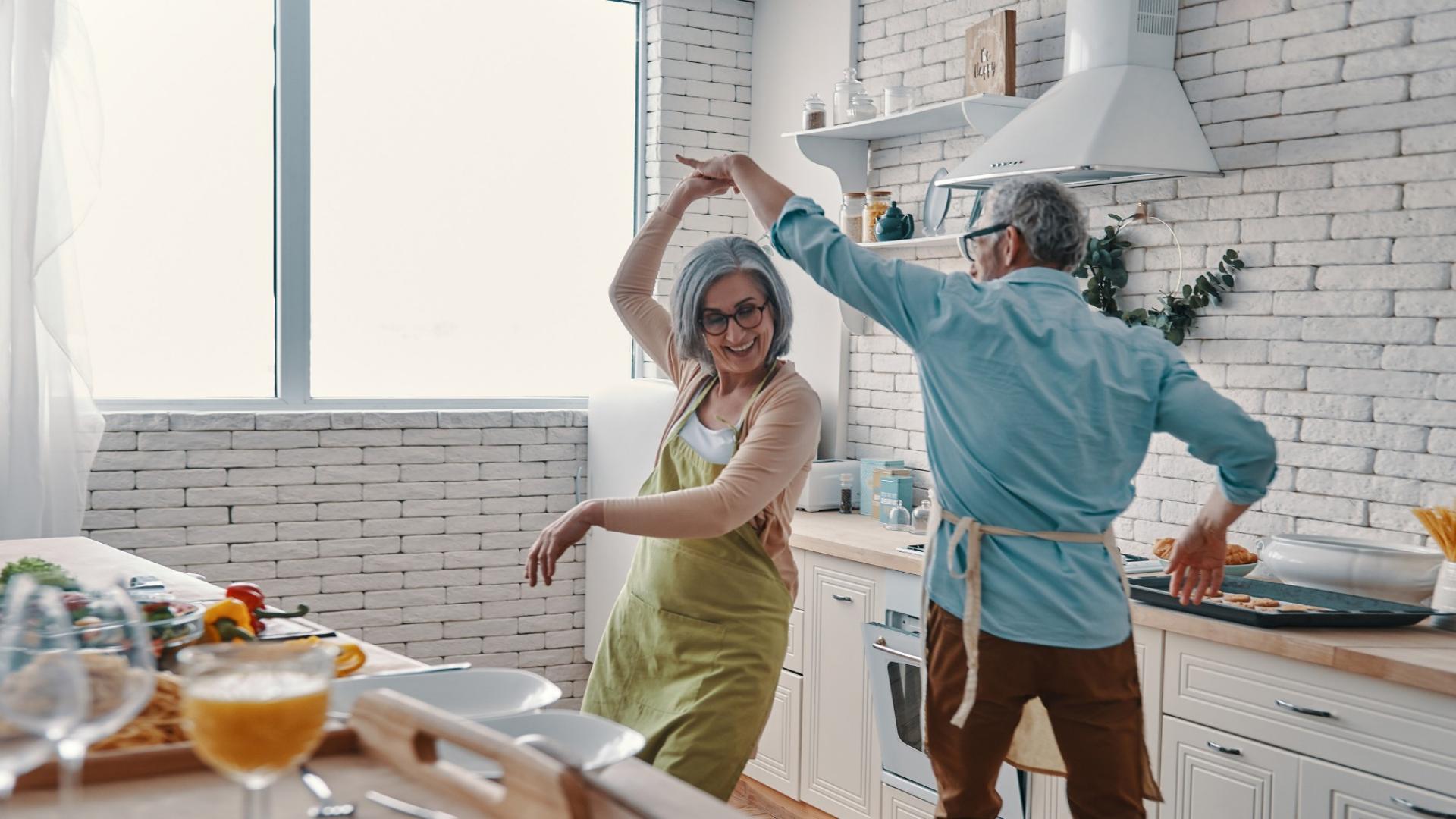 Auf dem Bild ist ein glückliches Pärchen abgebildet, das eine Sofortrente erhältz und in der Küche tanzt.