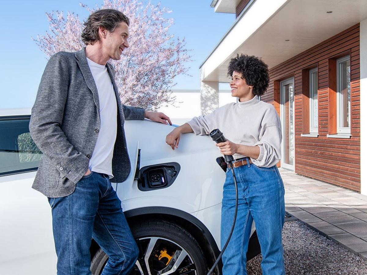 Das Bild zeigt eine Frau, die sich mit einem Mann unterhält und gerade ihr Elektroauto auflädt.