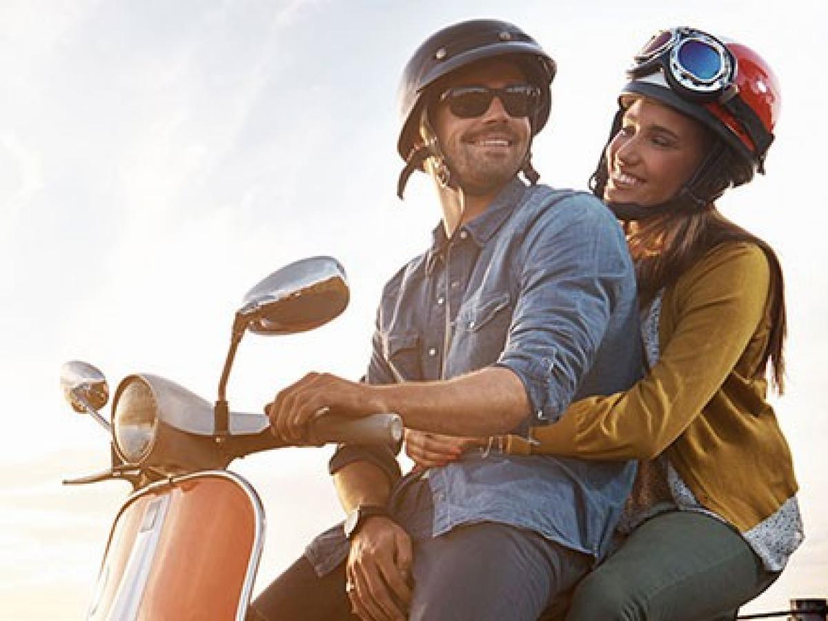 Ein junger Mann und eine junge Frau sitzen mit Helm auf einem Roller