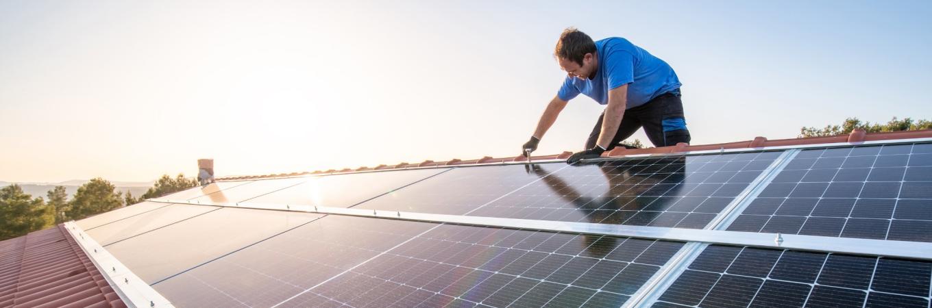 Ein Mann befestigt auf einem Dach eine Photovoltaikanlage.