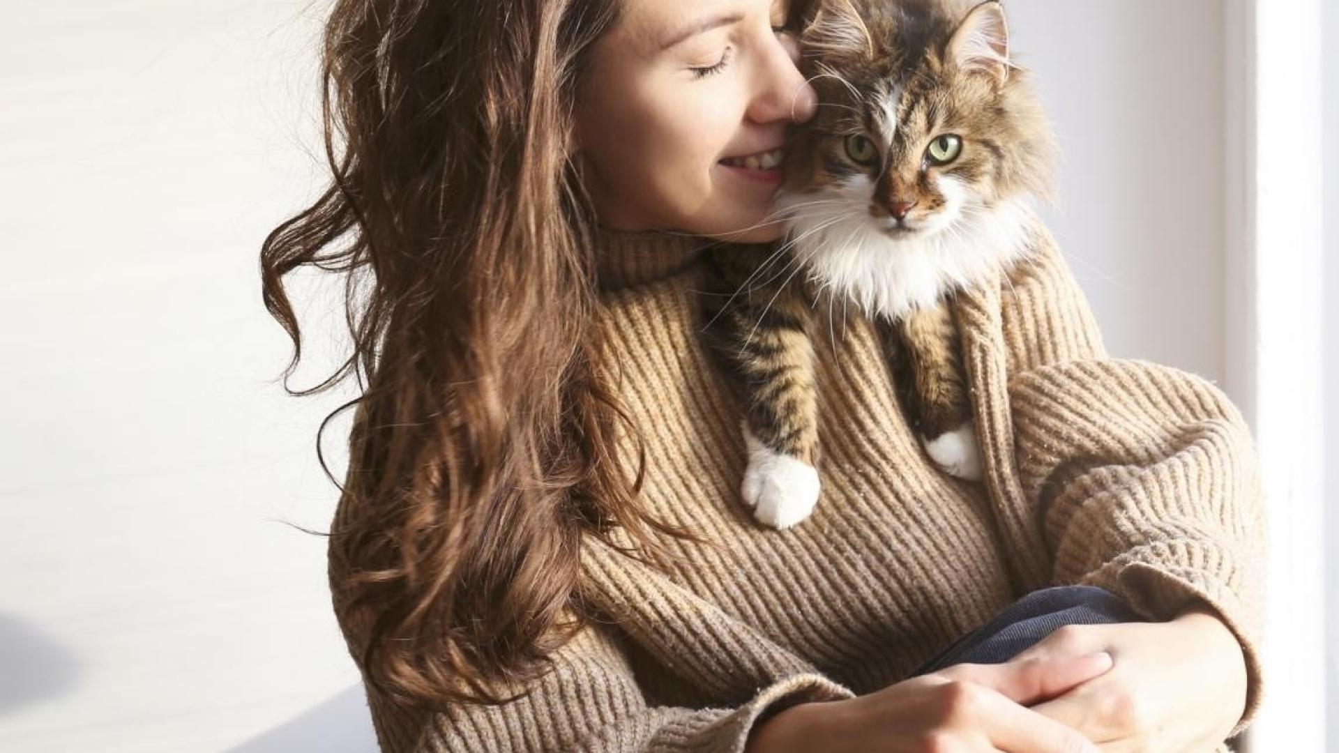 Auf der Schulter einer jungen Frau sitzt eine getiegerte Katze.