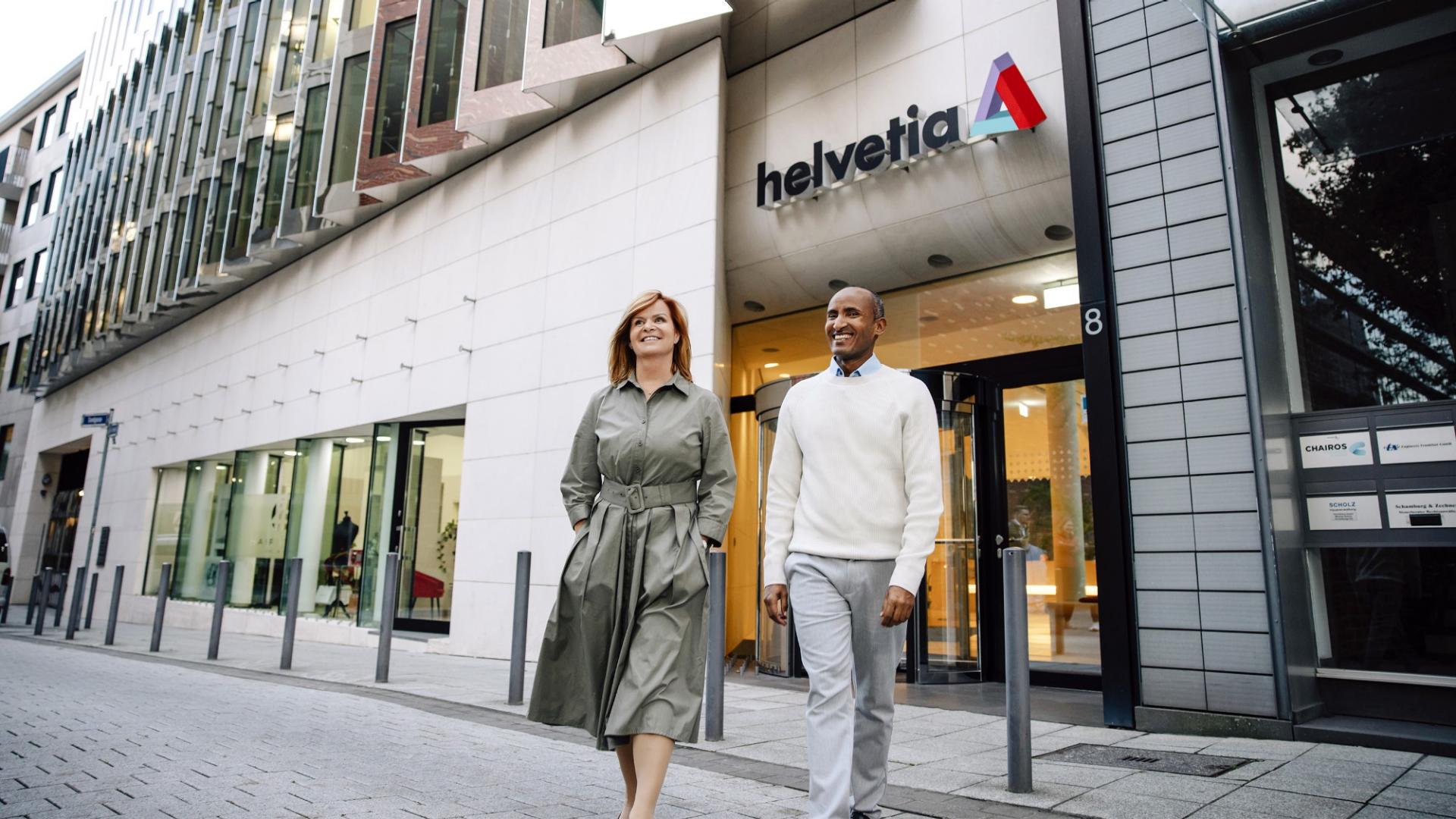 Ein Mann und eine Frau überqueren eine Straße vor der Helvetia-Zentrale