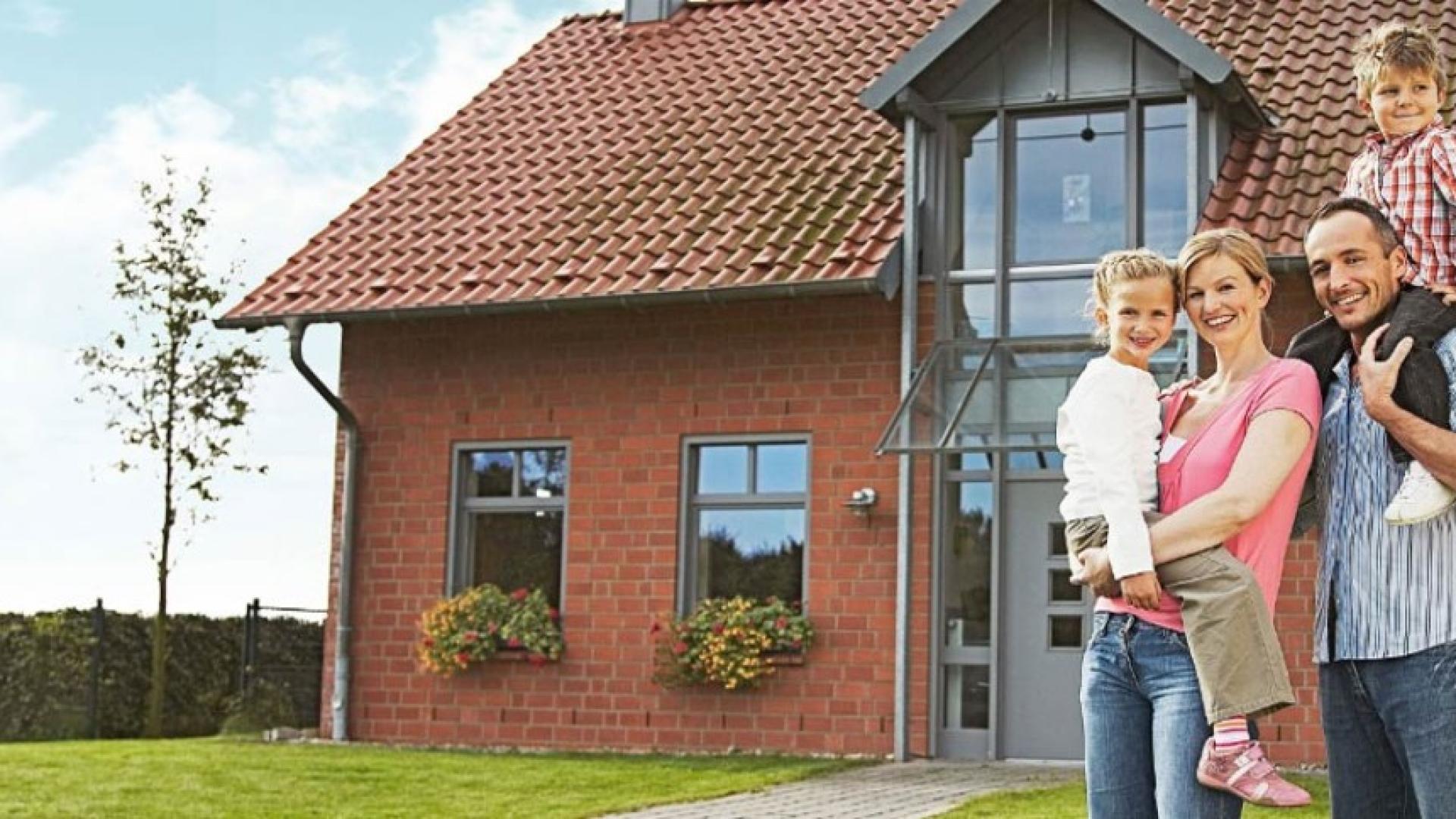 Vater, Mutter mit Baby sitzen vor einem Haus.
