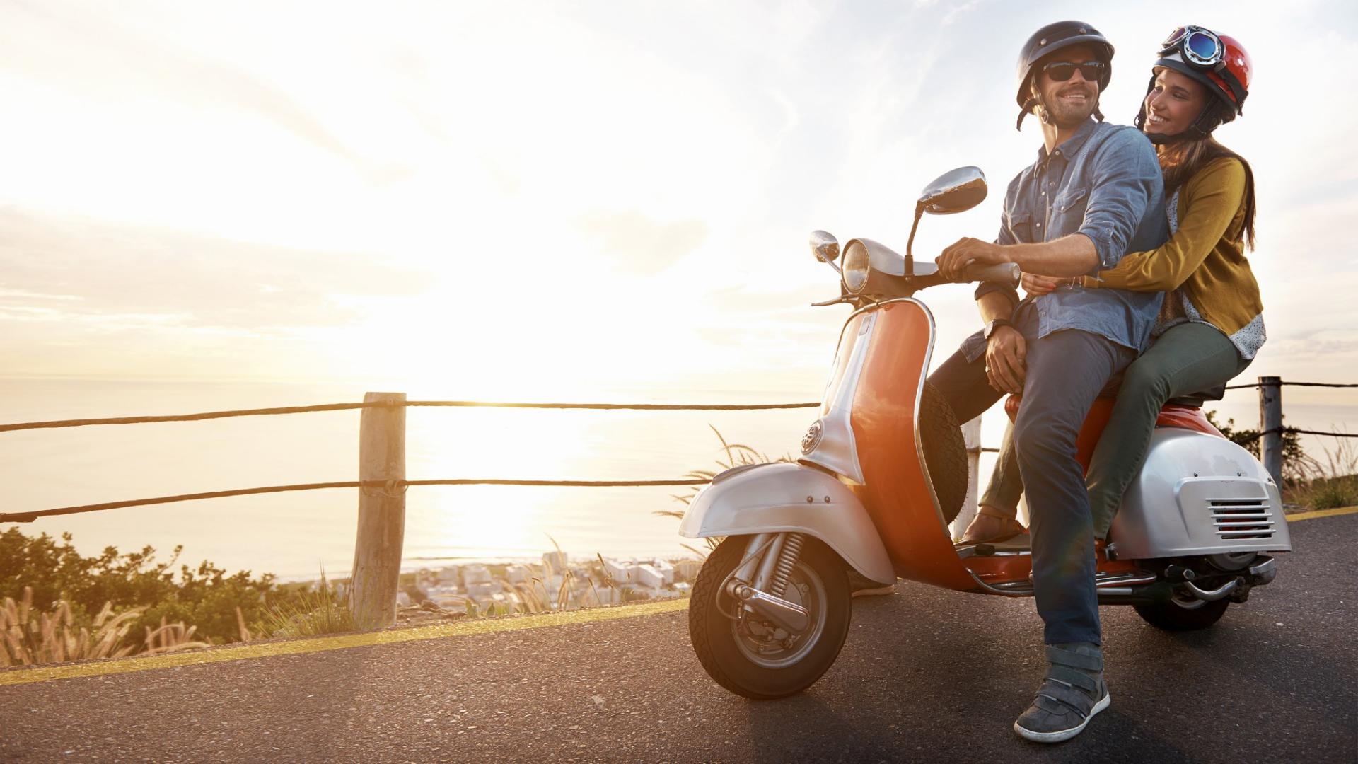 Ein Mann sitzt auf einem Roller und hinter ihm eine Frau, die sich an ihm festhält.