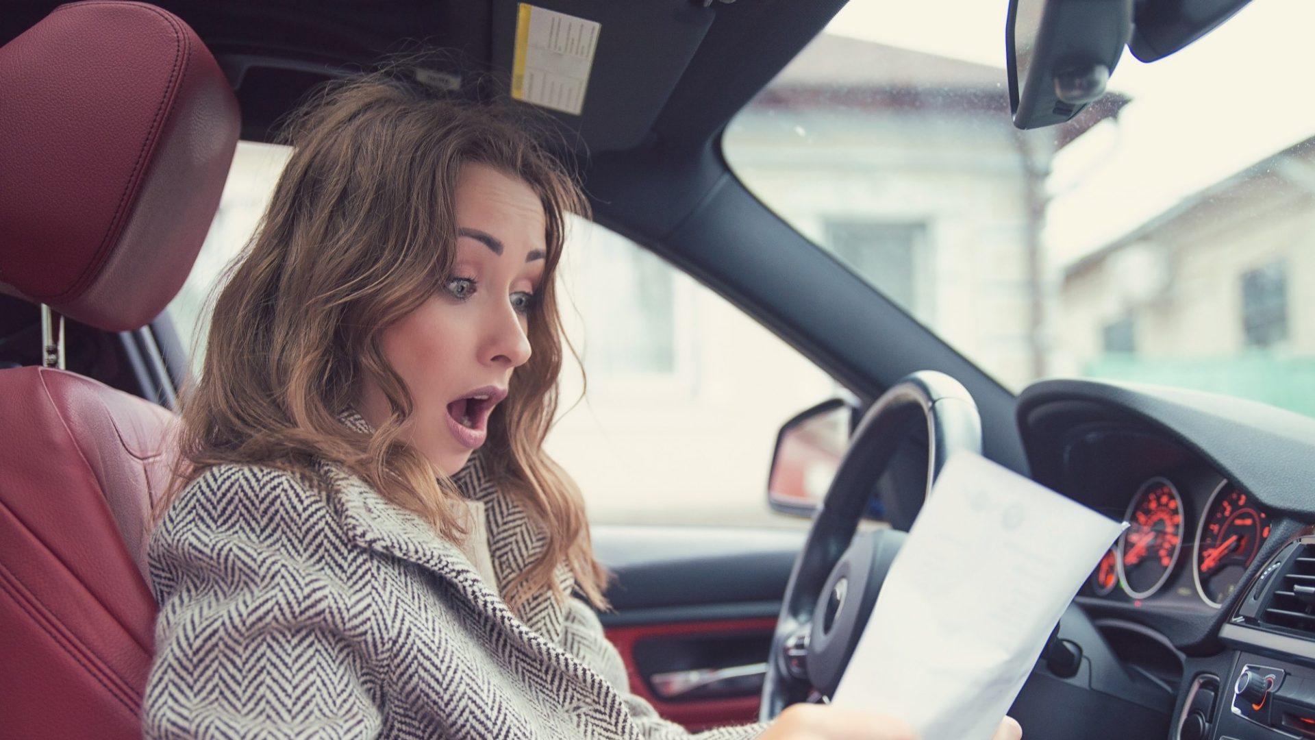 Shocked woman in car reading insurance paper